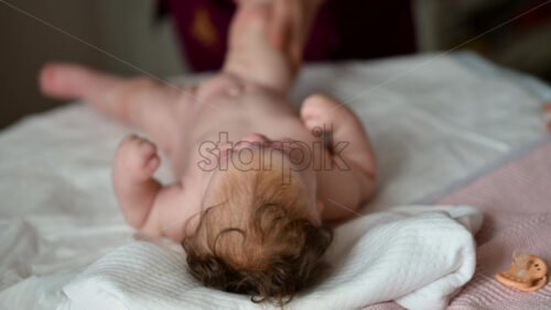 A newborn lying on a soft bed while a caregiver is massaging the baby