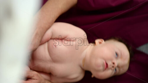 Baby sitting upright while being supported by a caregiver from behind. Vertical