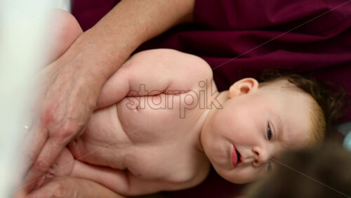 Baby resting on a caregiver's lap during a care routine. Vertical