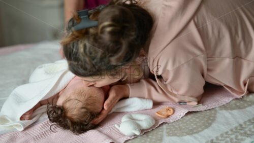 Mother leaning over her baby while assisting during a care routine on a bed