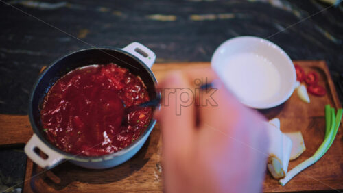 Close up of a spoon stirring borscht inside a small pot placed on a wooden board