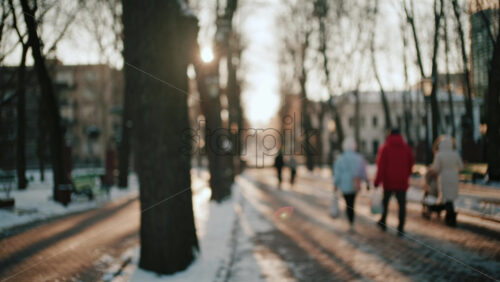 Out of focus view of people walking along a snowy park path during sunset