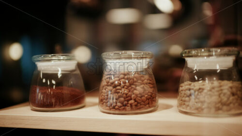 Close up of glass jars filled with different types of coffee beans displayed on a wooden shelf