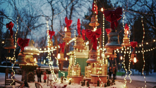 Decorative Christmas bells hanging above a festive market display with warm fairy lights and red bows
