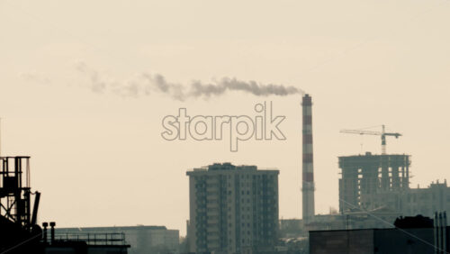 Urban skyline with residential buildings and an industrial chimney emitting smoke at sunset