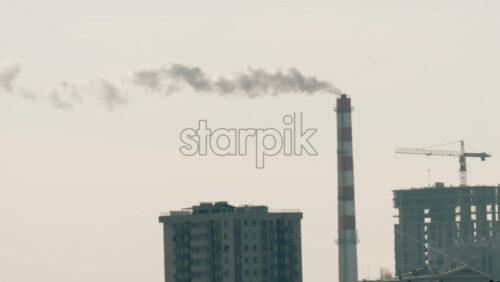 Urban skyline with residential buildings and an industrial chimney emitting smoke at sunset