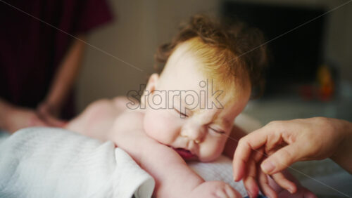 Close up of a baby while an adult gently supports them during a home care routine