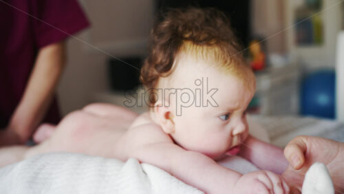 Close up of a baby while an adult gently supports them during a home care routine