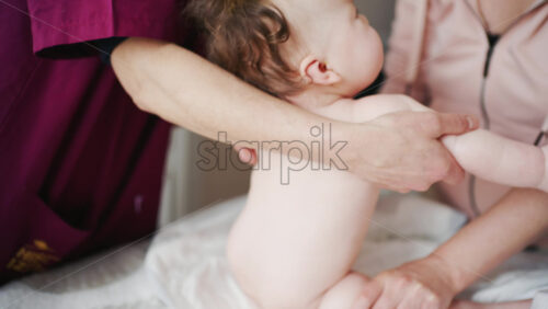 Adult gently lifting a baby into a supported upright position while the mother smiles