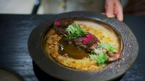Close up of a gourmet plated dish with sliced meat, rich sauce, and microgreens