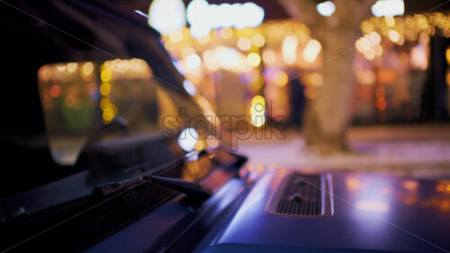 Close up of a vehicle hood reflecting warm golden city lights at night