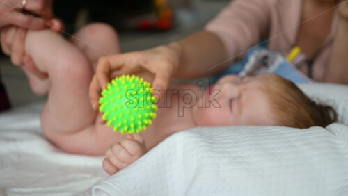 Infant interacting with a green, textured sensory ball, during mobility exercises