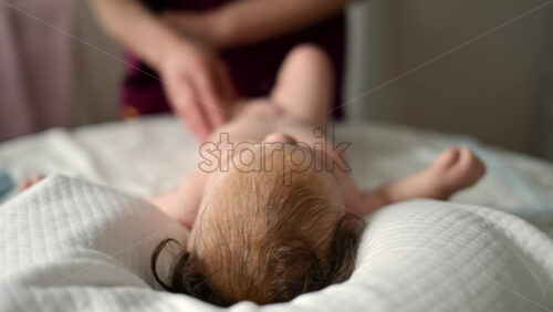 Adult hands gently massaging a baby lying on white sheets