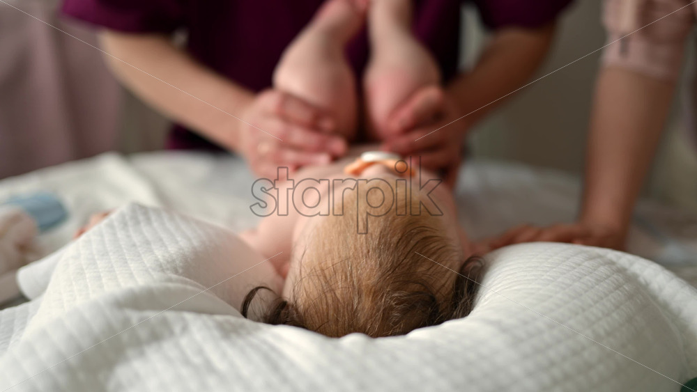 Adult hands gently massaging a baby lying on white sheets