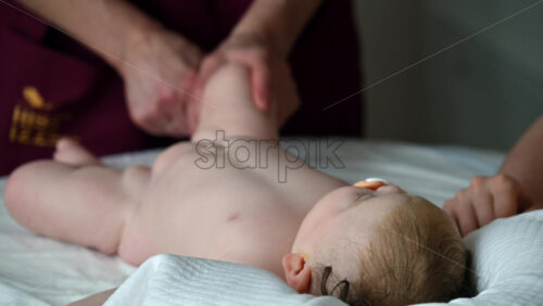 Infant lying relaxed on a bed, looking upward while a caregiver massages and performs mobility exercises