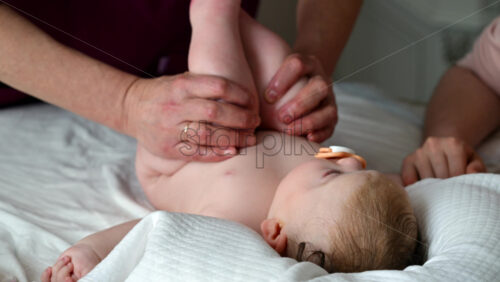 Baby lying on back with pacifier while adults assist with gentle leg movements
