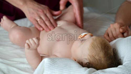Baby lying on their back while an adult massages them and the mother gently holds the baby's hand