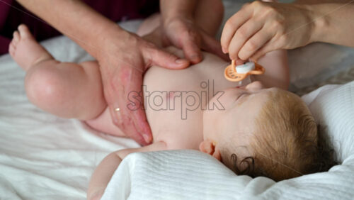 Baby lying on their back while an adult massages them and the mother gently holds the baby's hand