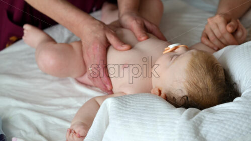 Baby lying on their back while an adult massages them and the mother gently holds the baby's hand