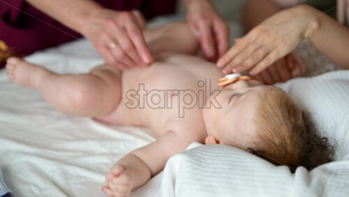 Baby lying on their back while an adult massages them and the mother gently holds the baby's hand