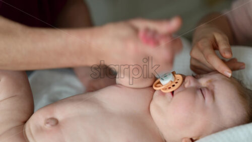 Baby lying on their back while an adult massages them and the mother gently holds the baby's hand