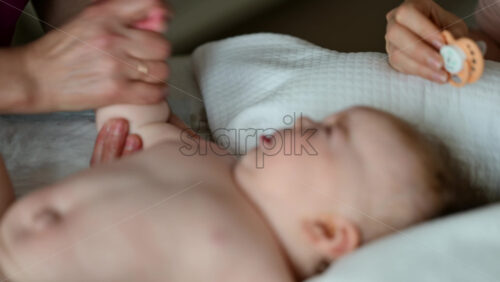 Baby lying on their back while an adult massages them and the mother gently holds the baby's hand