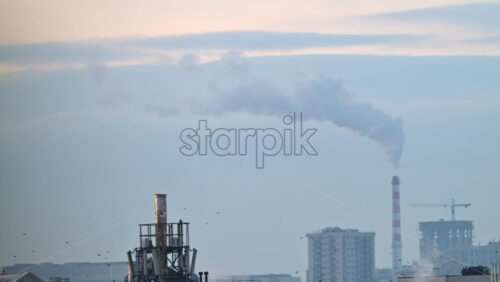 City rooftops on a cold winter day with multiple chimneys releasing white smoke into a pale sky