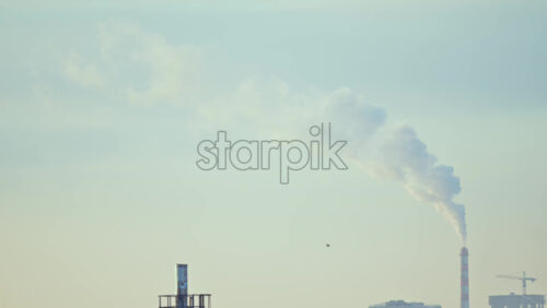City rooftops on a cold winter day with multiple chimneys releasing white smoke into a pale sky