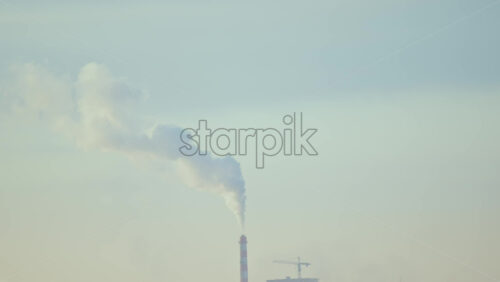 City rooftops on a cold winter day with multiple chimneys releasing white smoke into a pale sky