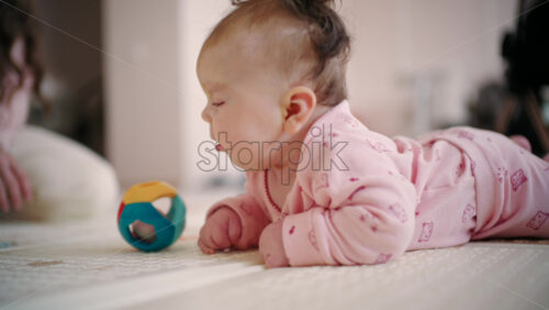Baby lying on tummy on a soft mat, facing a colorful geometric toy ball