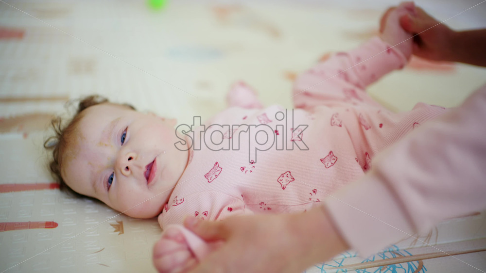 Close view of caregiver's hands supporting the baby's legs while the infant curls slightly