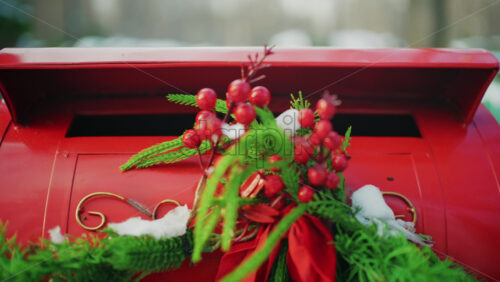 Close up of a festive red mailbox decorated with evergreen branches, red berries, and light snow
