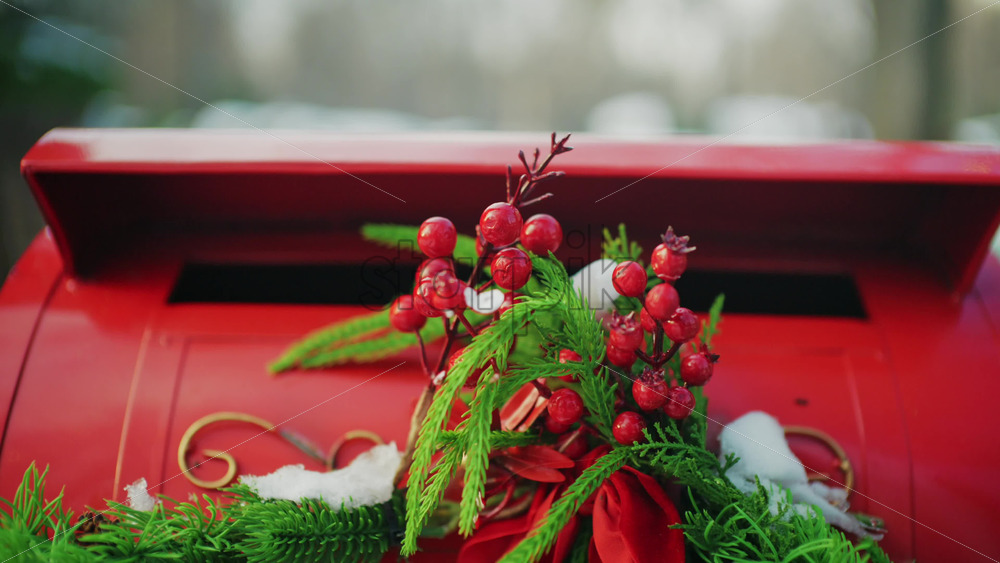 Close up of a festive red mailbox decorated with evergreen branches, red berries, and light snow