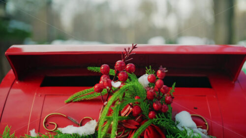 Close up of a festive red mailbox decorated with evergreen branches, red berries, and light snow