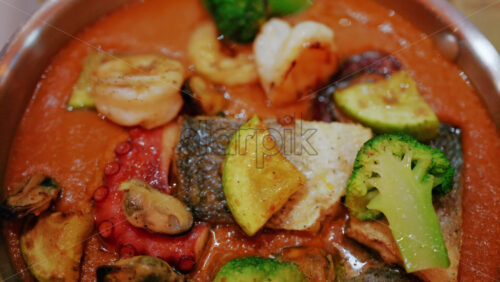Close up of a gourmet seafood dish in a rich sauce with fish, octopus, shellfish, and vegetables
