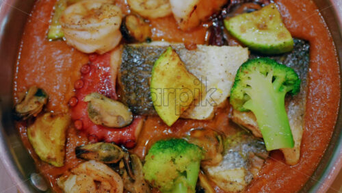 Close up of a gourmet seafood dish in a rich sauce with fish, octopus, shellfish, and vegetables