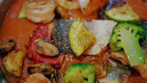 Close up of a gourmet seafood dish in a rich sauce with fish, octopus, shellfish, and vegetables