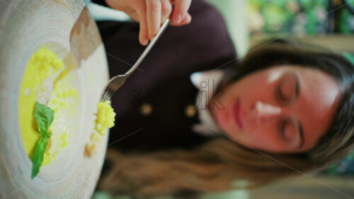 Close up of a woman eating risotto with greens at a restaurant. Vertical