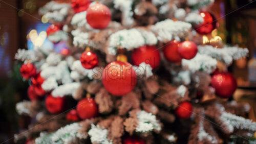 Decorated Christmas tree with red ornaments, snow covered branches, and soft glowing lights in the background