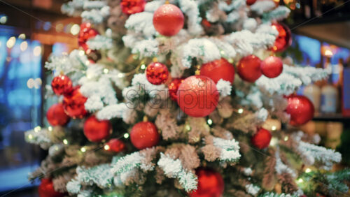 Decorated Christmas tree with red ornaments, snow covered branches, and soft glowing lights in the background