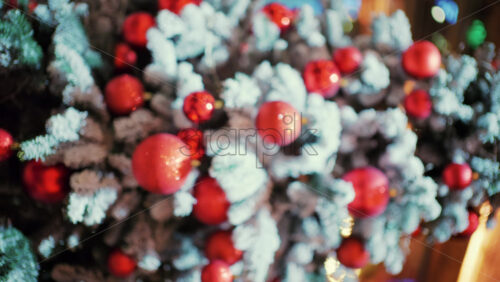 Snow dusted evergreen branches decorated with red Christmas ornaments and warm string lights. Vertical