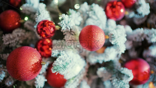 Snow dusted evergreen branches decorated with red Christmas ornaments and warm string lights. Vertical