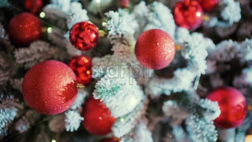 Snow dusted evergreen branches decorated with red Christmas ornaments and warm string lights. Vertical