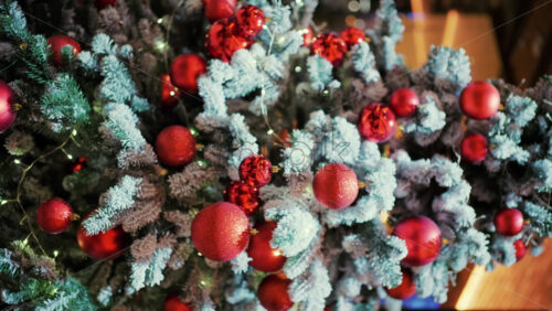Snow dusted evergreen branches decorated with red Christmas ornaments and warm string lights. Vertical