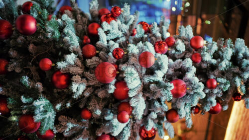 Snow dusted evergreen branches decorated with red Christmas ornaments and warm string lights. Vertical