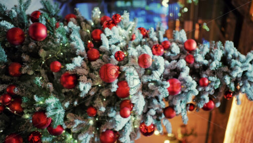 Snow dusted evergreen branches decorated with red Christmas ornaments and warm string lights. Vertical