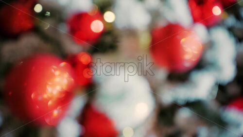Close up of a decorated Christmas tree with red ornaments, snow covered branches, and soft glowing lights in the background