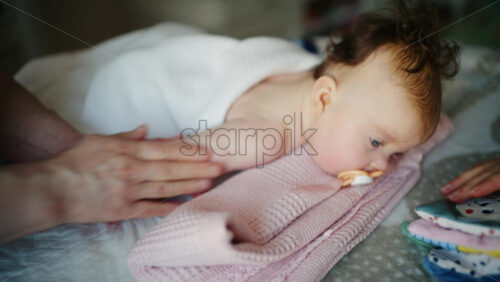 Baby lying on their back while an adult massages them and the mother holds the pacifier in the baby's mouth