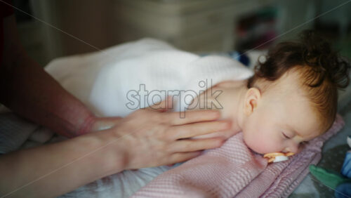 Baby lying on their back while an adult massages them and the mother holds the pacifier in the baby's mouth