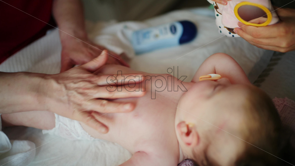 Infant lying on back while an adult gently rubs lotion or oil onto the baby's body